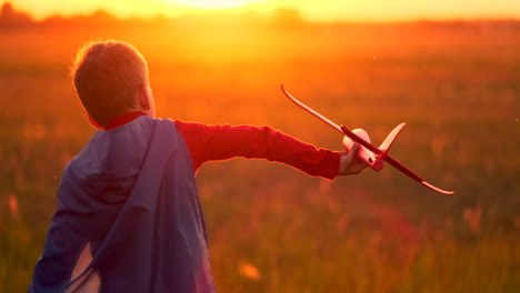 Boy-pilot-runs-in-a-red-raincoat-holding-a-plane-laughing-at-sunset-in-the-summer-field-imagining-that-he-is-an-airplane-pilot-playing-with-a-model-airplane